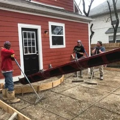 Crew screeding fresh concrete for a patio behind a red house
