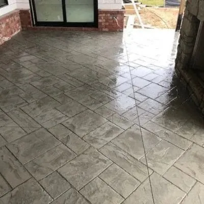 Gray stamped slate-pattern concrete floor under a covered porch with a stone fireplace